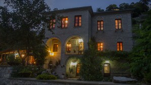 Un edificio de piedra con varios ventanales arqueados y un balcón, rodeado de vegetación.