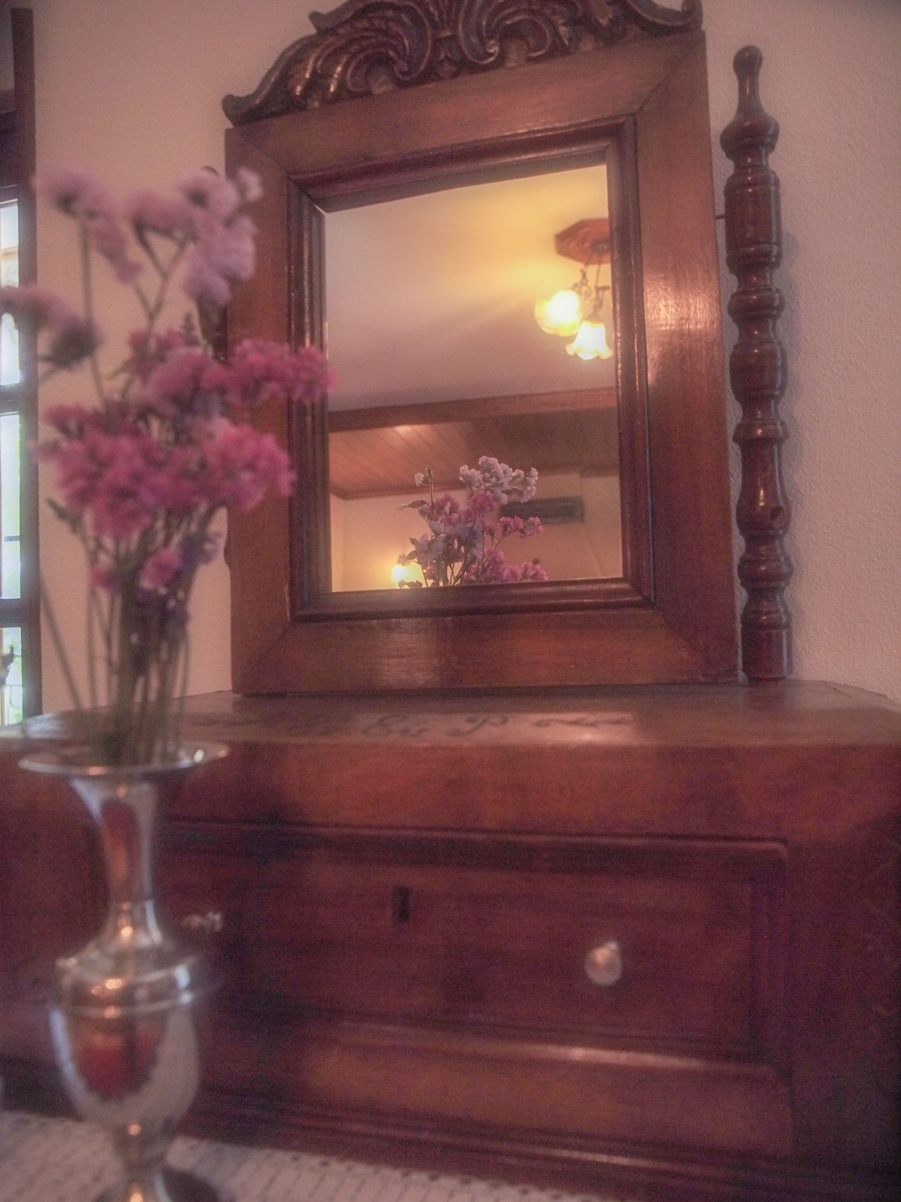 Une commode en bois avec un miroir, un vase de fleurs et une lampe.