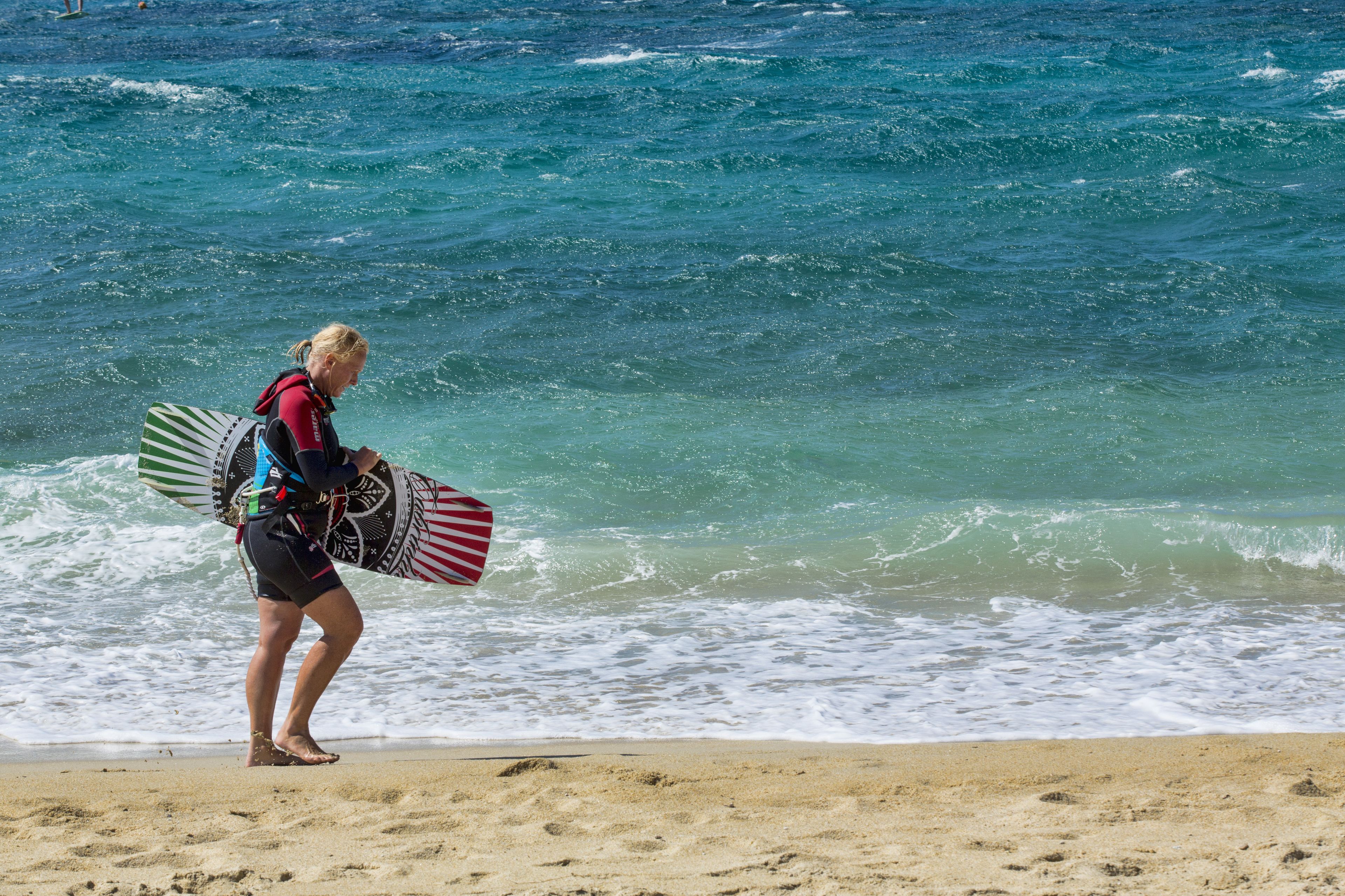 Une personne qui porte une planche de surf sur une plage, avec des vagues en arrière-plan.