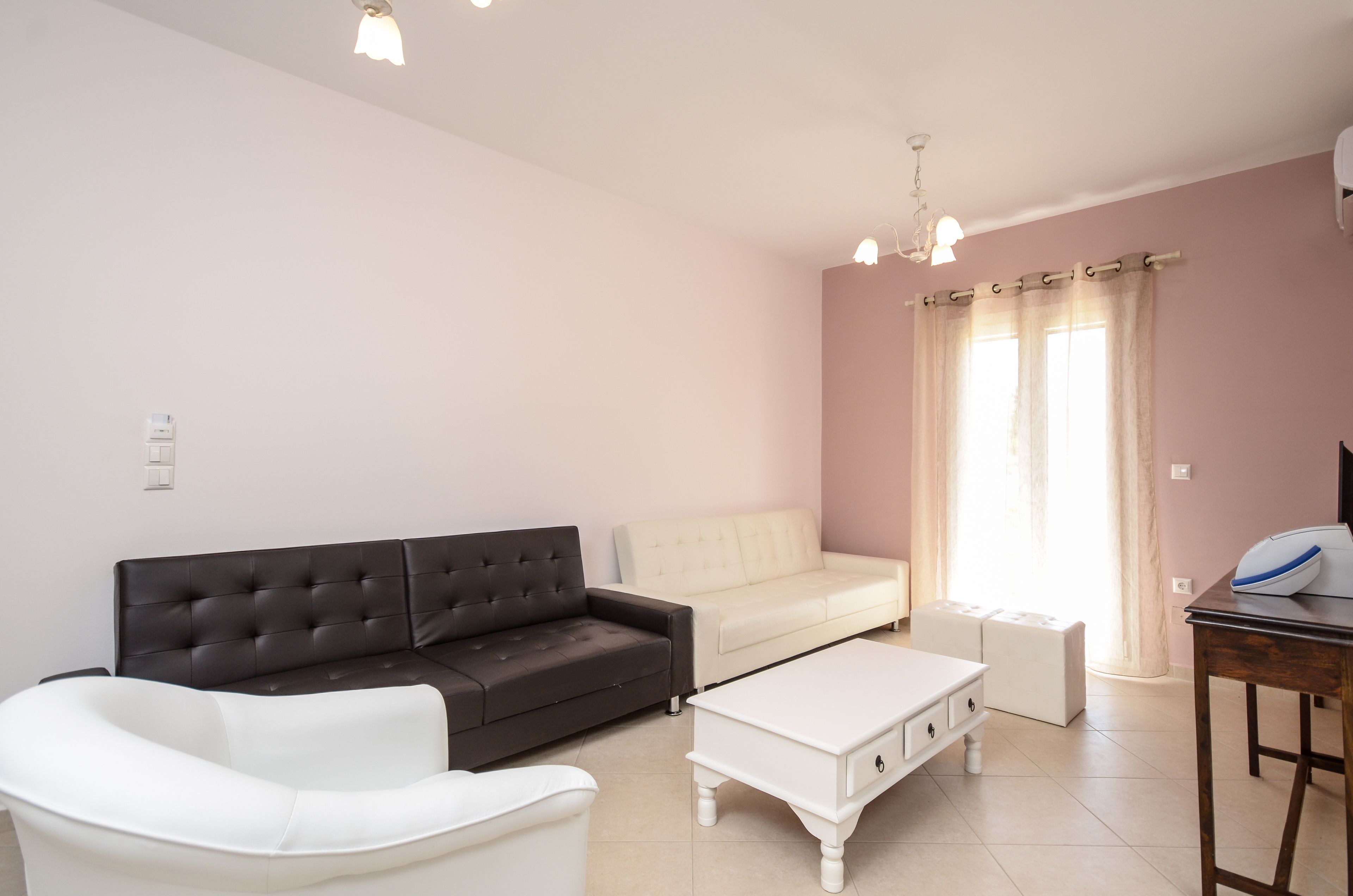 Una sala de estar con un sofá blanco y negro, un sillón blanco, una mesa de centro blanca y una mesita con un dispositivo.
