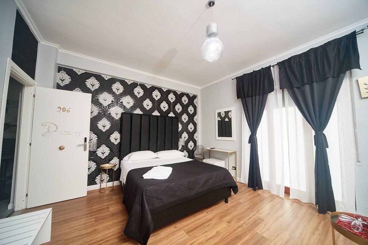 Um quarto com cama, mesa de cabeceira, abajur e porta.