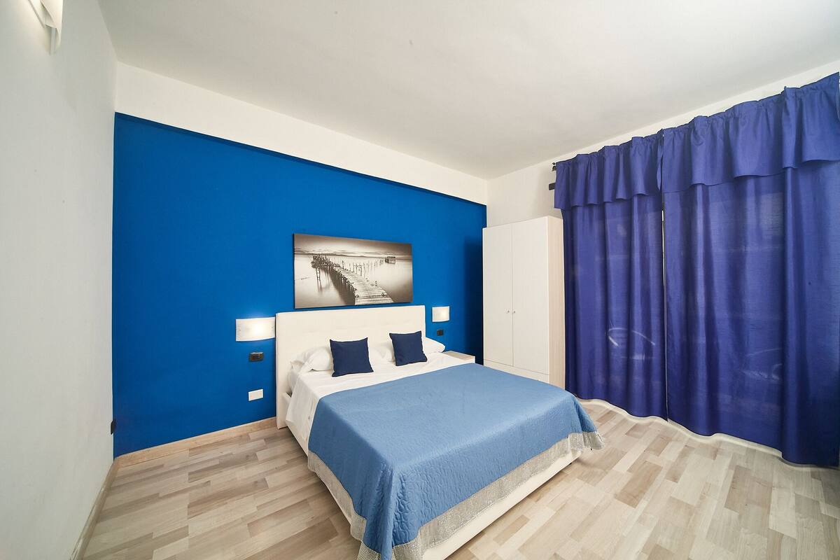 Quarto com cama, parede azul e janela com cortinas azuis.