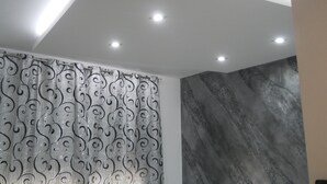 Une salle de bain avec un luminaire au plafond, un rideau de douche à motifs et un mur à texture.