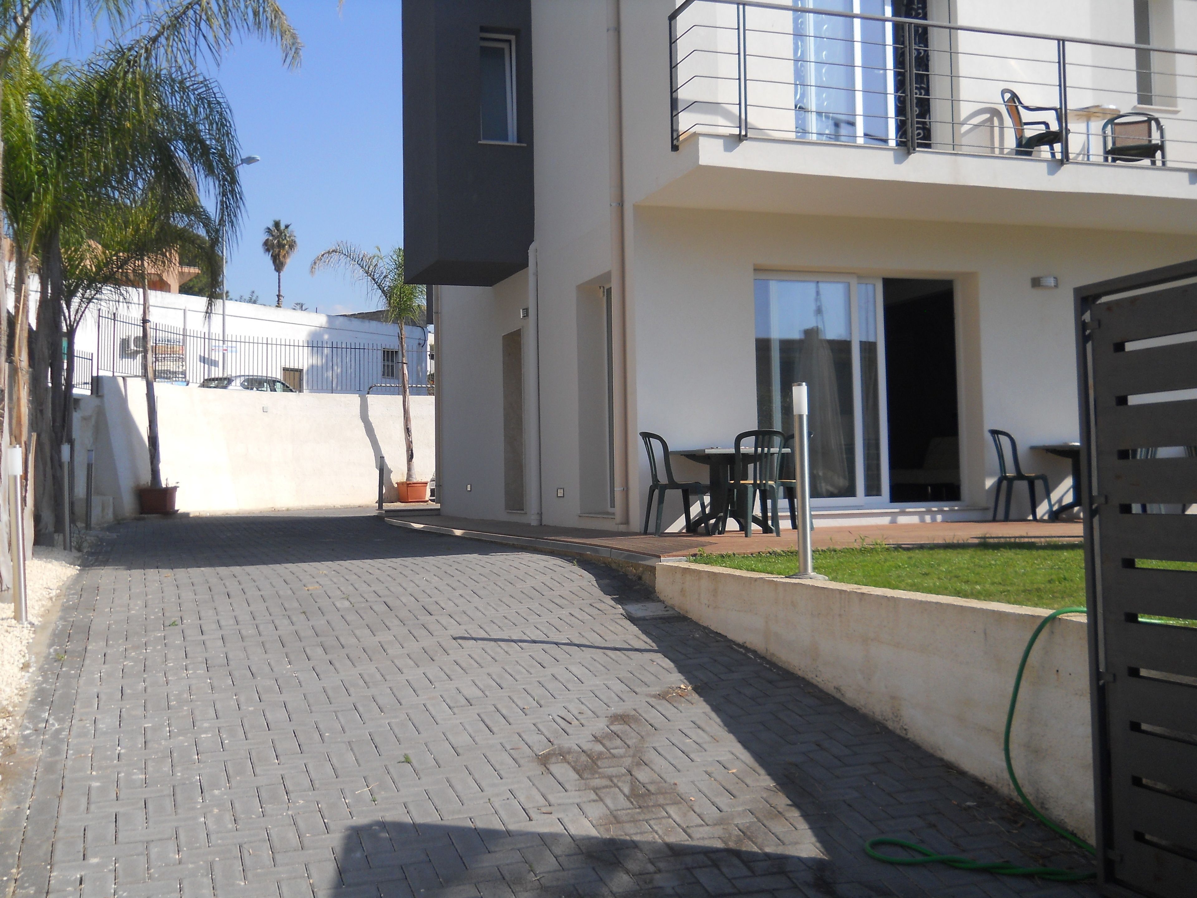 Ein gepflasterter Innenhof mit Sitzgelegenheit, ein Gebäude mit Balkon und ein klarer Himmel.
