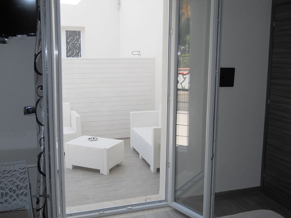 A room with a sliding glass door leading to an outdoor seating area with white wicker furniture.