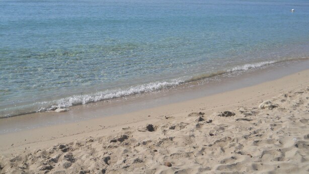 Une plage de sable fin, avec une eau d’un bleu limpide et une côte qui s’étend au loin.