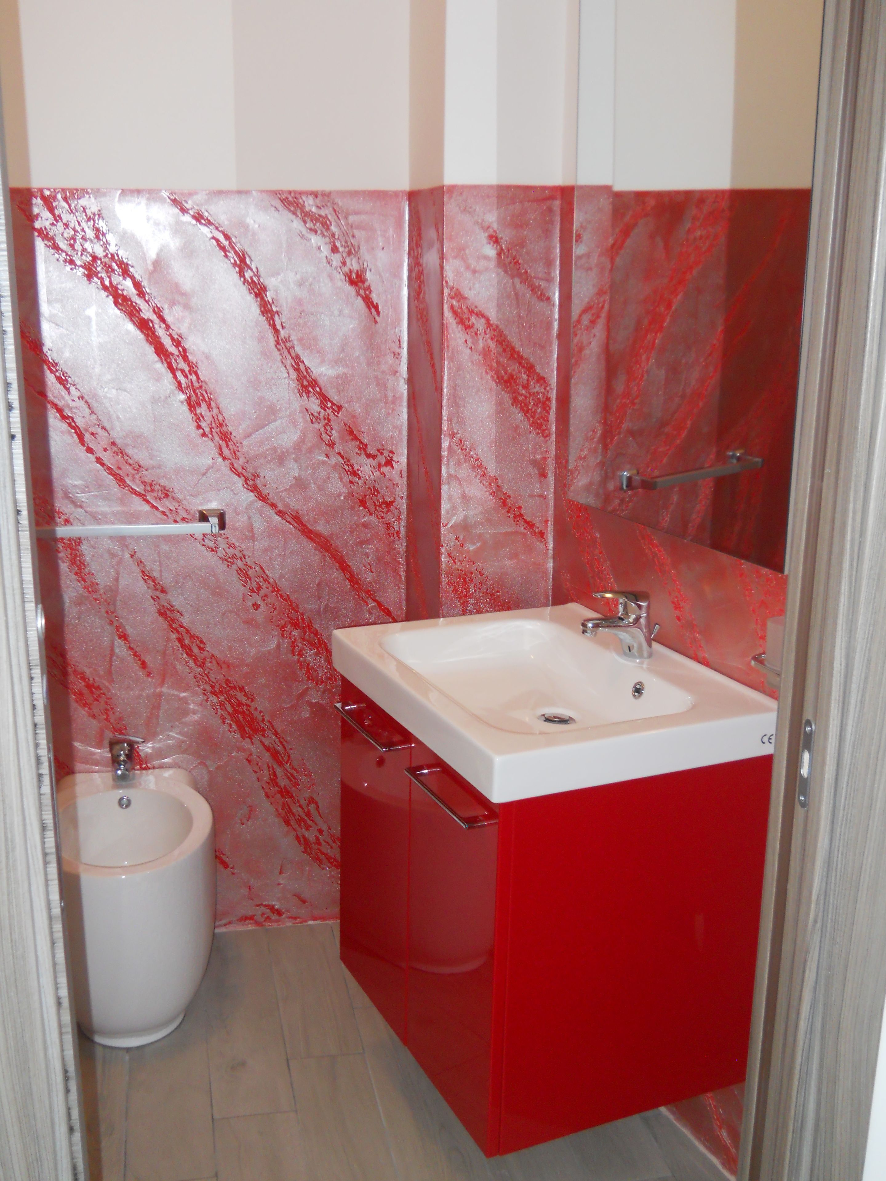 Une salle de bain avec un lavabo rouge, un miroir et des toilettes.