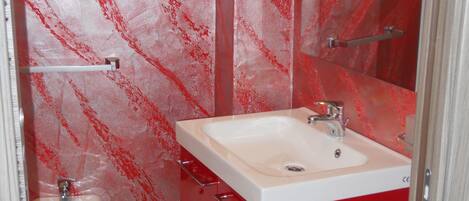 Une salle de bain avec un lavabo rouge, un miroir et des toilettes.
