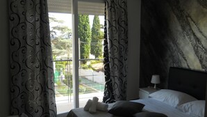 Une chambre d’hôtel avec un lit, des oreillers, une table de chevet, une lampe et une vue sur un balcon agrémenté de verdure.