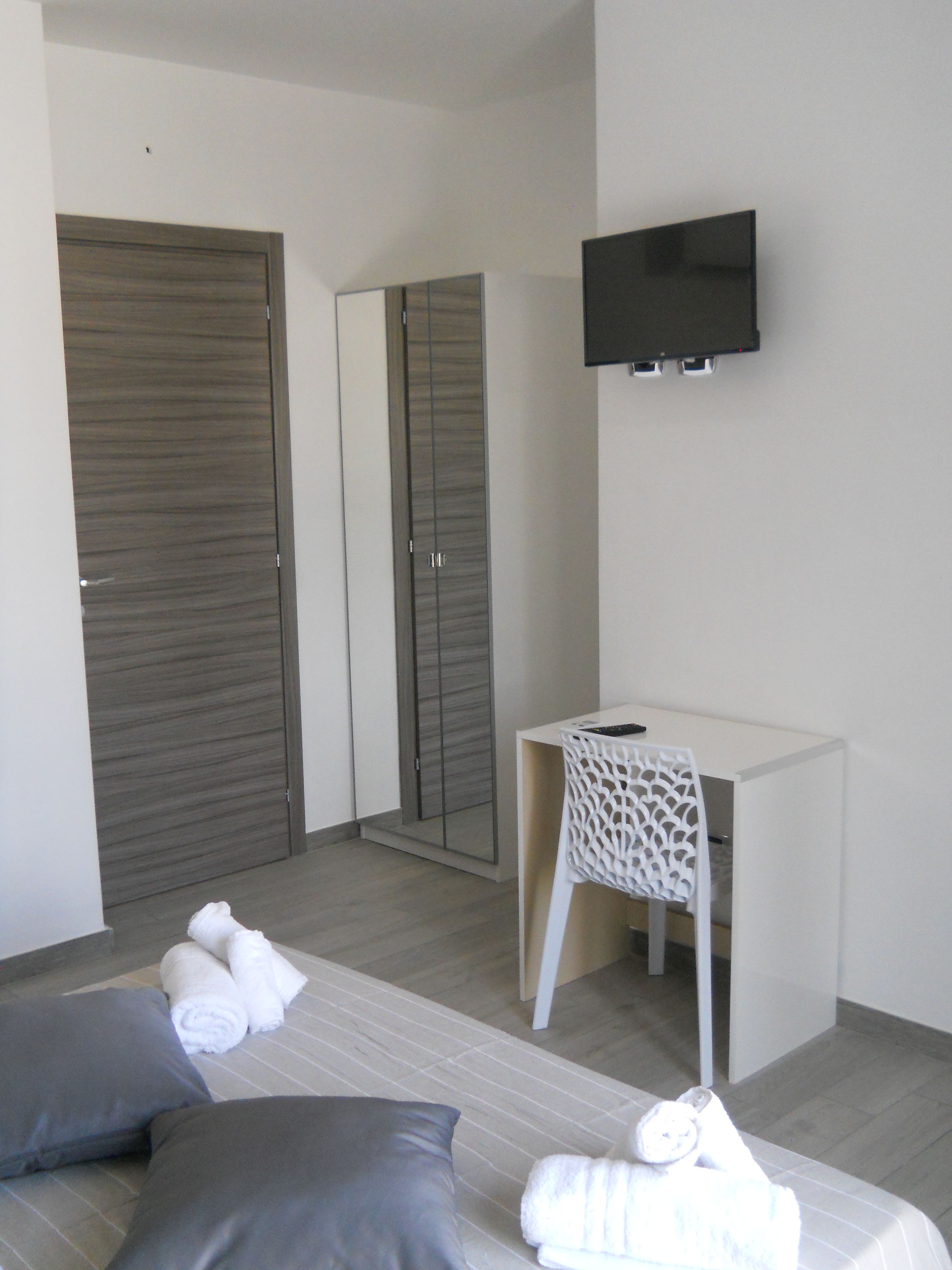 A hotel room with a bed, two pillows, a desk with a chair, a flat-screen TV, and a wardrobe.