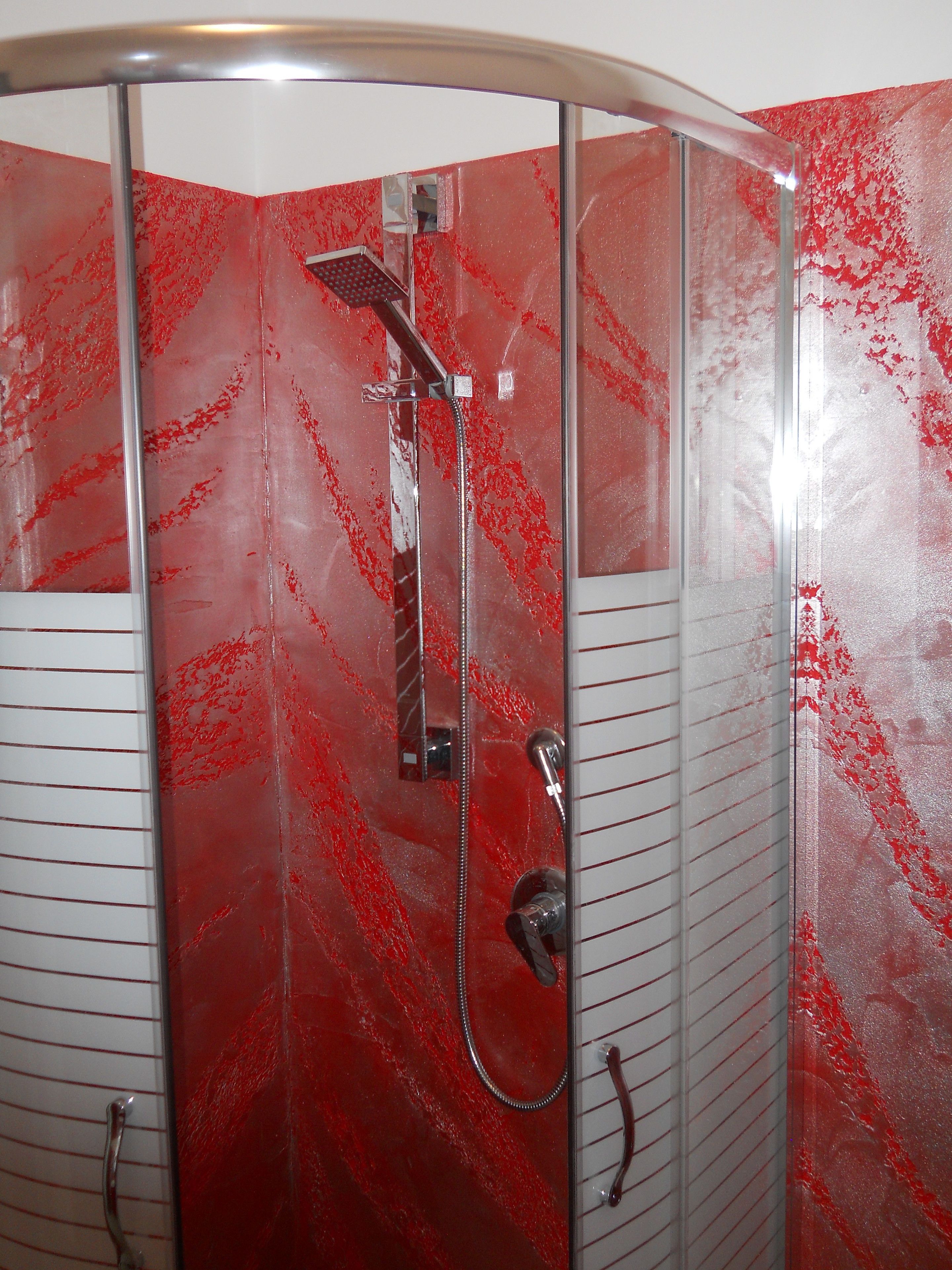 A shower with a glass door and a red marble-like wall.