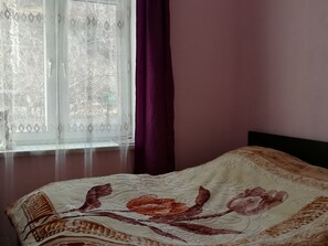 A bedroom with a bed, a window with lace curtains, and a purple curtain.
