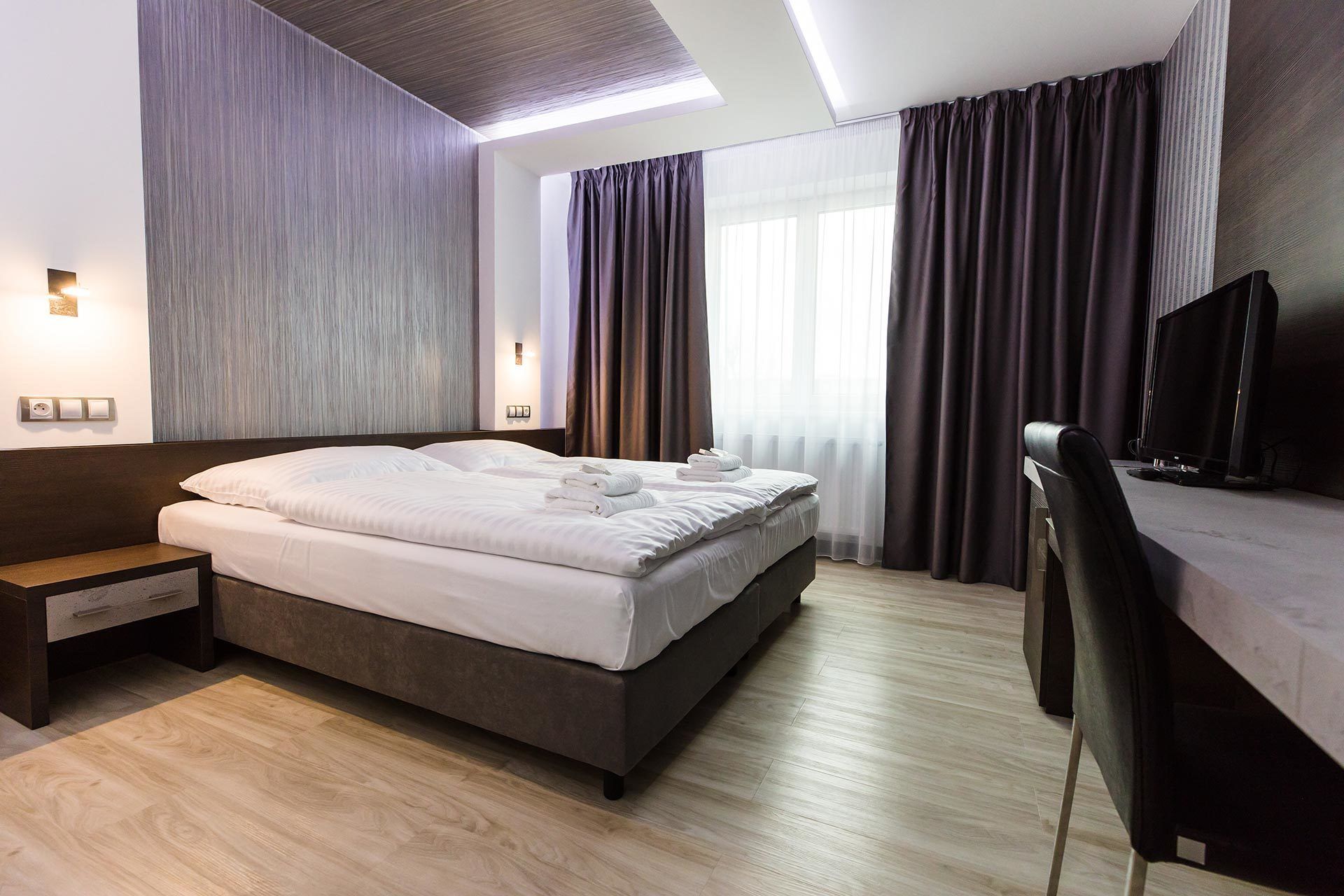 A modern hotel room with a large bed, a desk with a computer, and a TV.