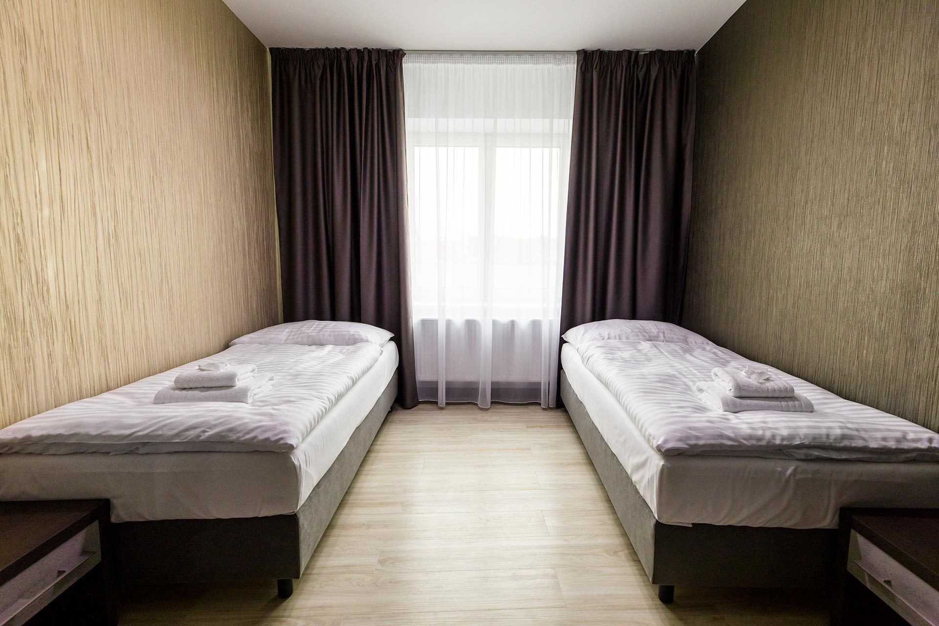 Une chambre avec deux lits simples, une fenêtre avec des rideaux légers et un plancher en bois.