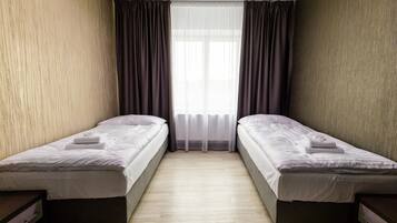 Una habitación con dos camas individuales, una ventana con cortinas traslúcidas y suelo de madera.