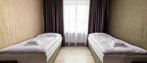 Una habitación con dos camas individuales, una ventana con cortinas traslúcidas y suelo de madera.