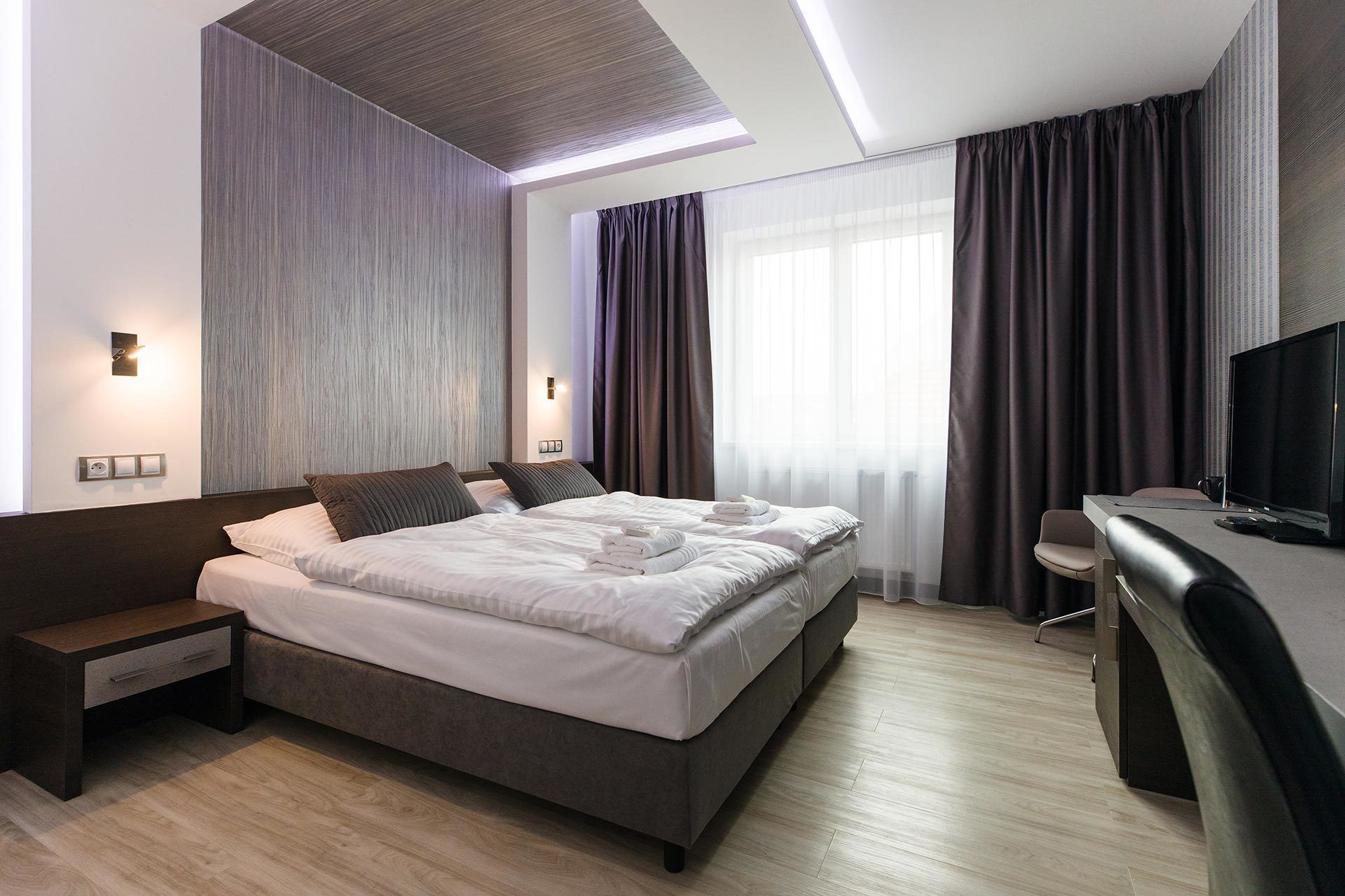 Una habitación de hotel moderna con una cama grande, mesitas de noche, un escritorio con silla y televisión.