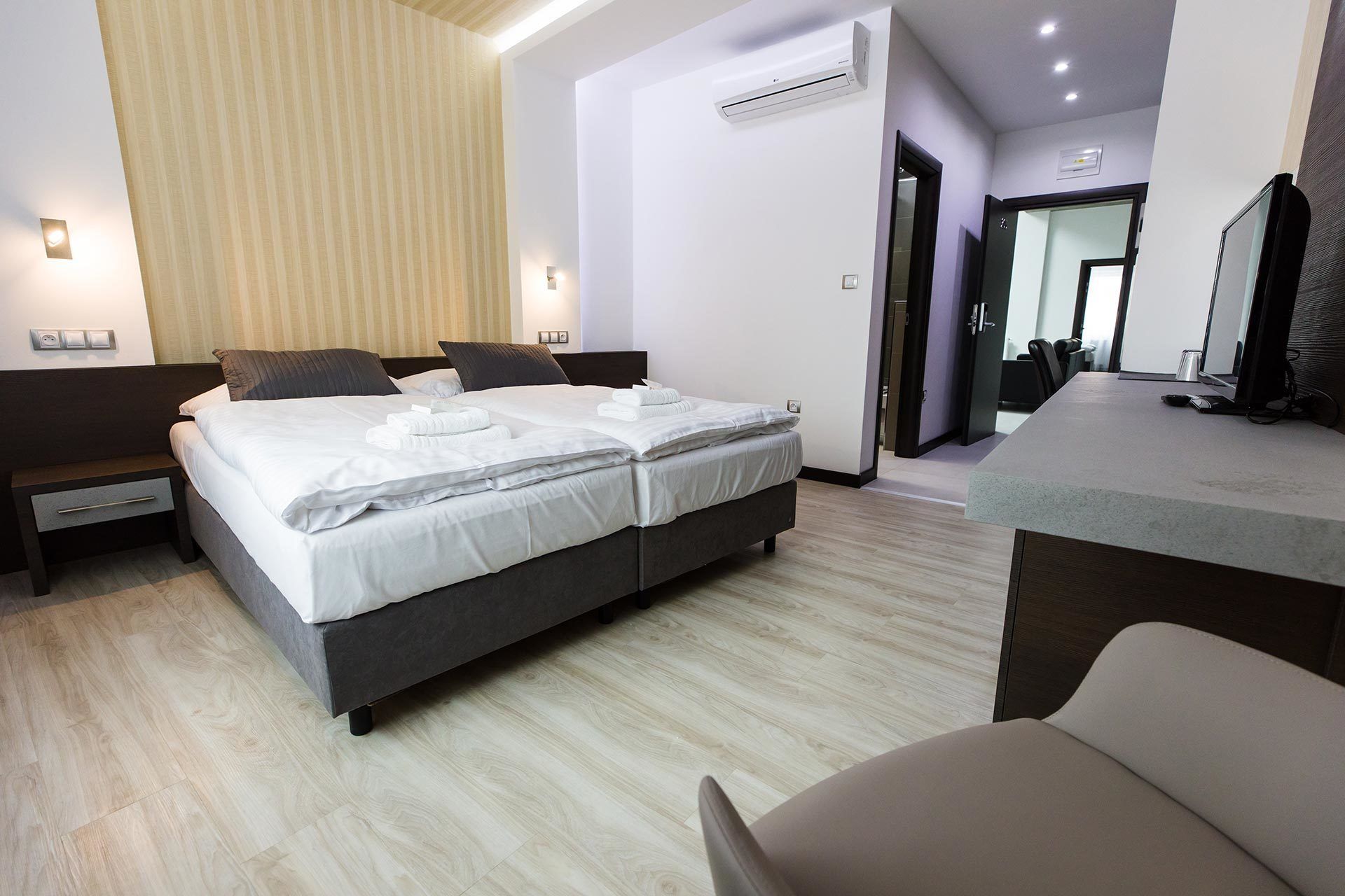 A modern hotel room with a large bed, bedside tables, a desk, and an air conditioning unit.