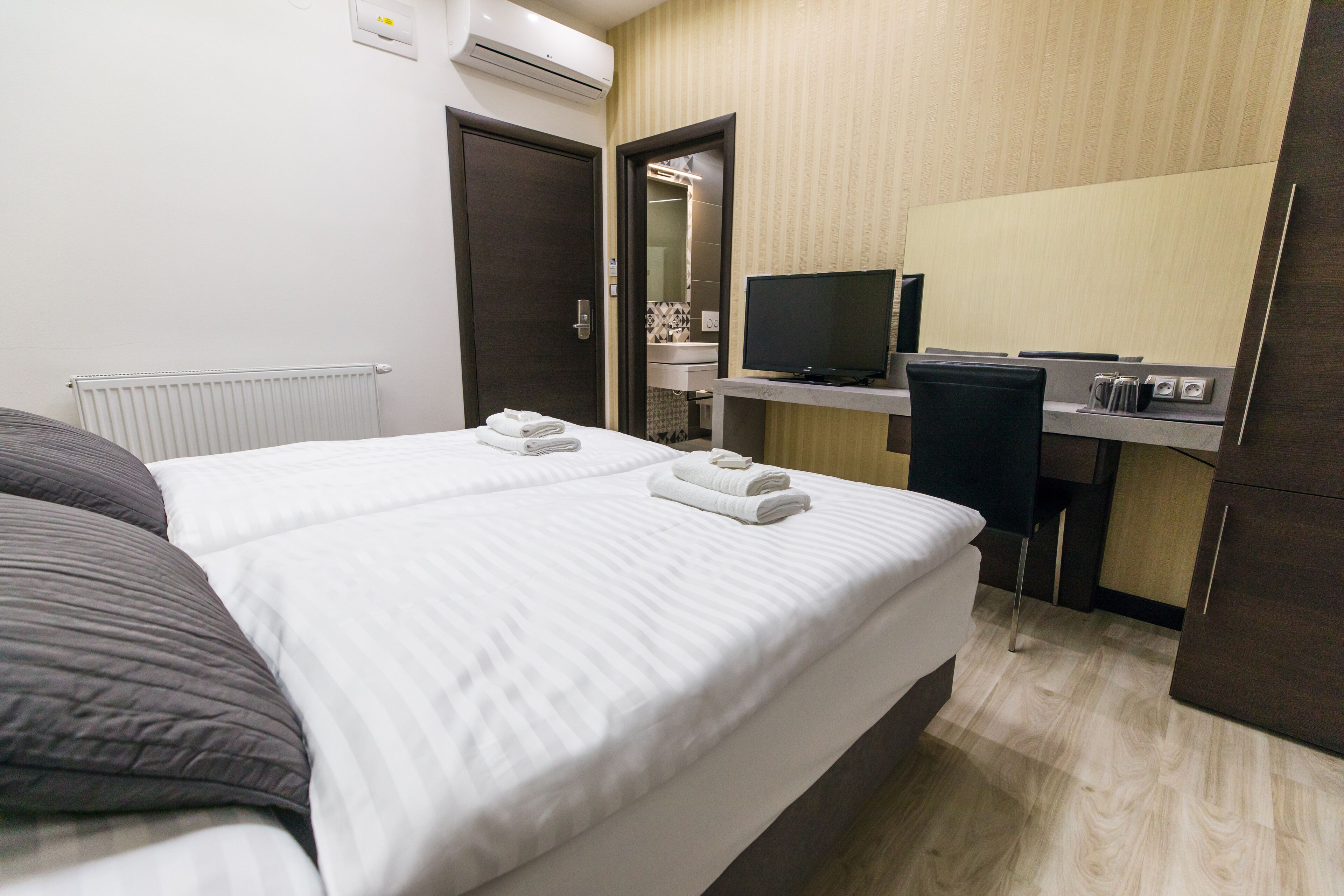 Habitació d'hotel amb un llit, escriptori amb ordinador, televisió i bany visible a través d'una porta oberta.