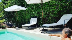 A man relaxing by a pool with two sun loungers and umbrellas, surrounded by greenery. - Hotel Las Chirimoyas  (Salta)