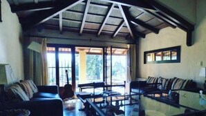 A spacious living room with a high ceiling, large windows, and a glass coffee table. - Hotel Las Chirimoyas  (Salta)