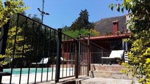 A fenced pool area with lounge chairs and a stone staircase leading to a building with a red roof. - Hotel Las Chirimoyas  (Salta)