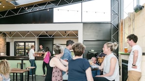 An outdoor seating area with tables and chairs, a bar with a bartender, and a stage with musical instruments. - The Cally Hotel (Warrnambool)