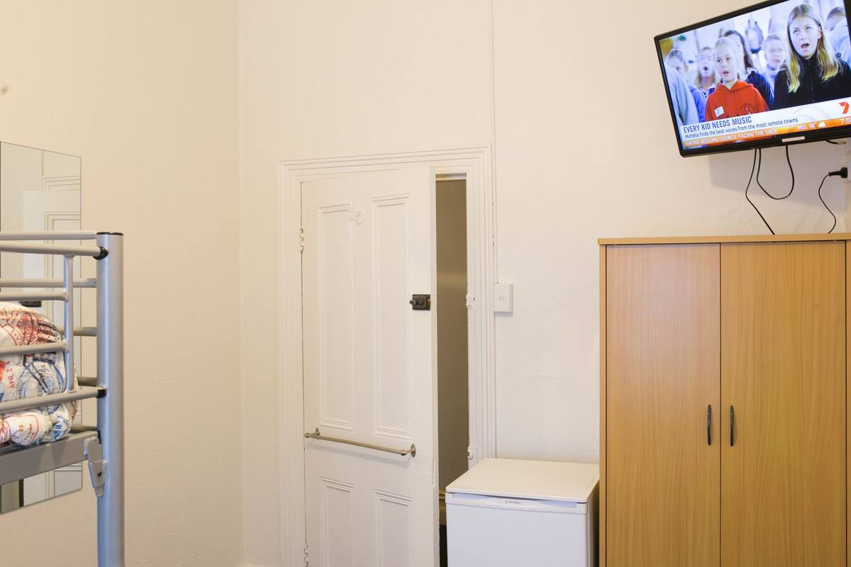 A room with a bunk bed, a white door, a wooden cabinet, and a television displaying a news channel.
