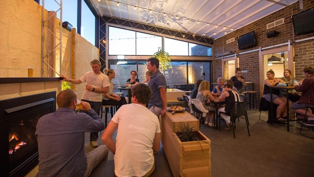 An indoor social space with a fireplace, wooden seating, and a large window. - The Cally Hotel (Warrnambool)
