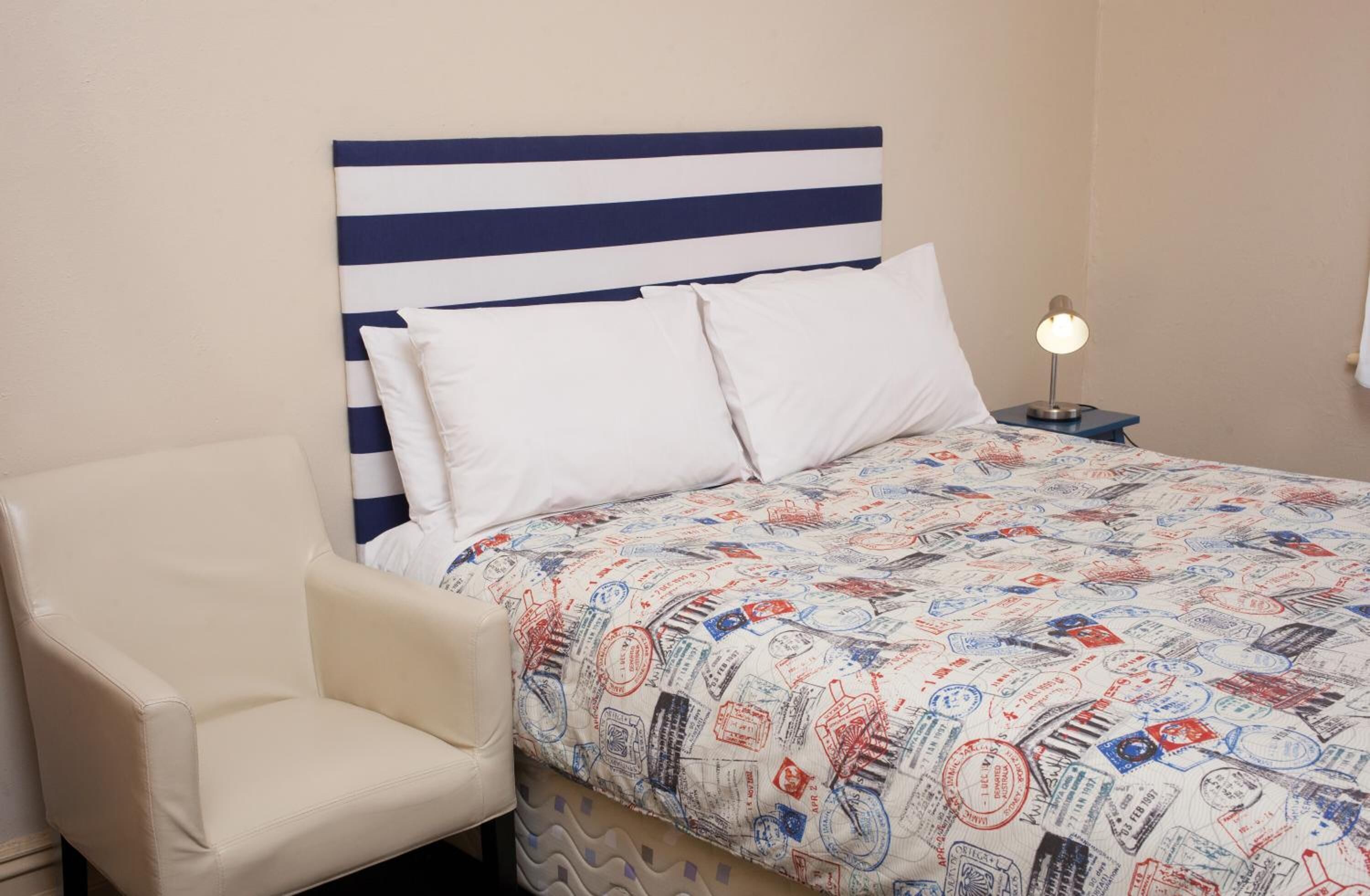 A bedroom with a striped headboard, a bed with a patterned duvet, a bedside lamp, and a chair.