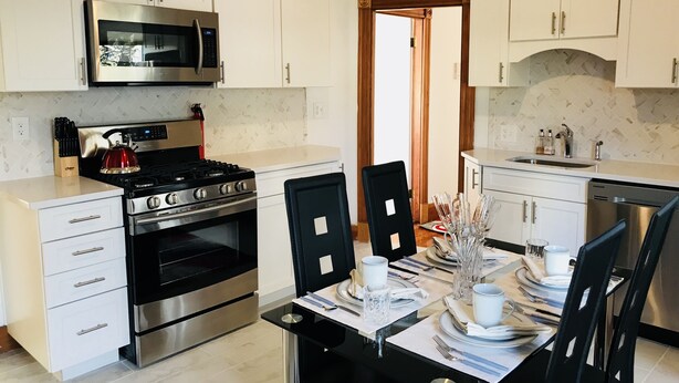 A modern kitchen with white cabinetry, stainless steel appliances, and a dining area set for six. - Lg suite for up to 8 ppl/3 floor (Boston)