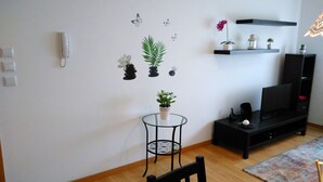 Ein Wohnzimmer mit einem schwarzen TV-Schrank, einem kleinen runden Tisch mit einem Blumentopf und einer Wand mit Schmetterlingsstickern.