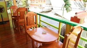 A wooden table and chairs in a room with a green railing and a view of the outside.