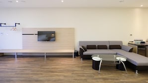A modern living room with a sectional sofa, a glass coffee table, and a flat-screen TV mounted on a wooden wall. - Yu Chun Hotel (Taichung)