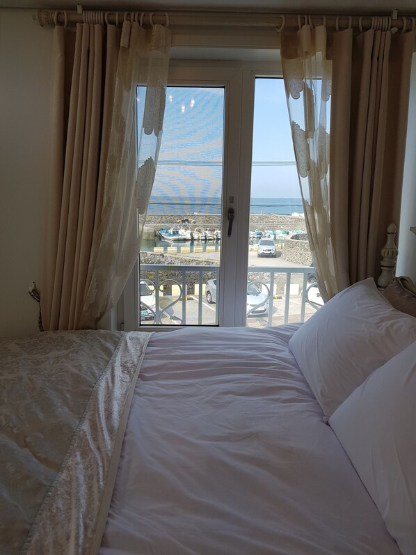 A bedroom with a bed, curtains, and a view of the beach and boats.