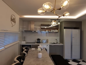 A modern kitchen with a marble countertop, a built-in oven, a refrigerator, and a unique light fixture.