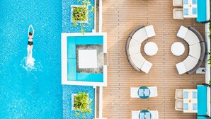 Vue aérienne d’un espace piscine avec des chaises longues et des tables, entouré d’une terrasse en bois.