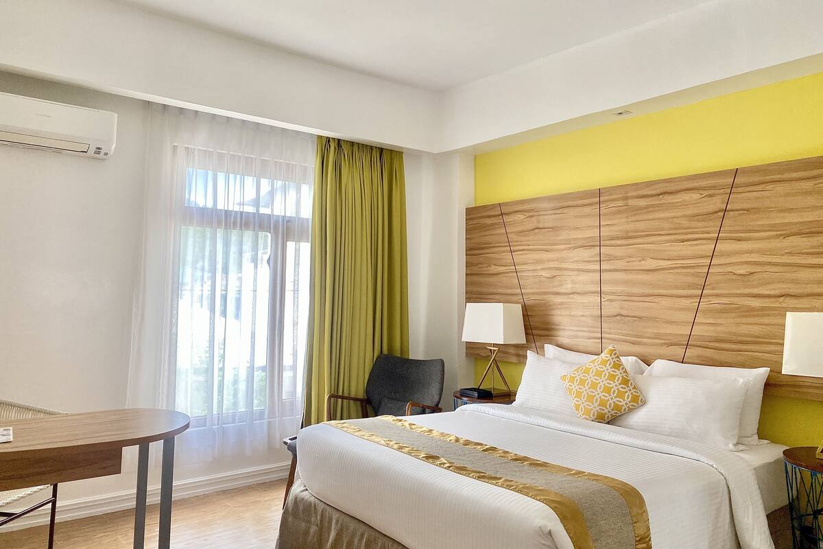 Ein Hotelzimmer mit Bett, Schreibtisch, Stuhl und einem fensterbepflanzten Fenster.