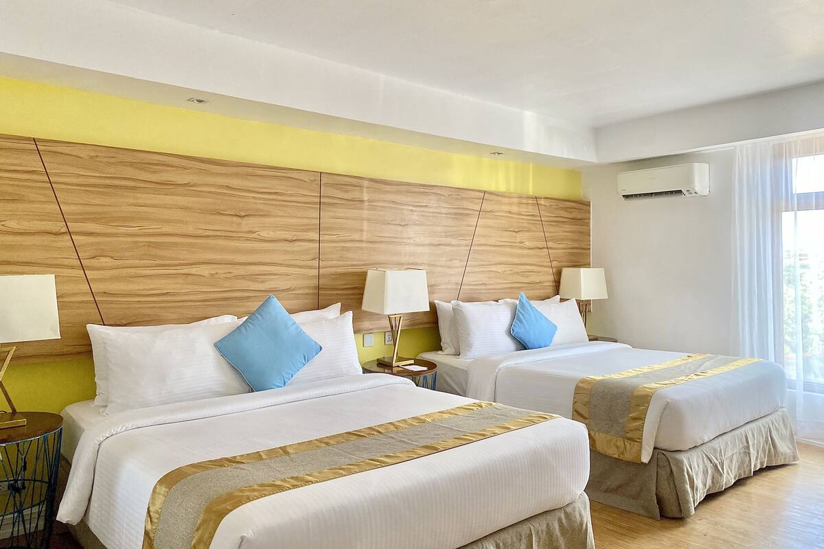 Ein Hotelzimmer mit zwei Betten, einem Holzkopfteil, Nachttischlampen und einem großen Fenster mit Vorhängen.