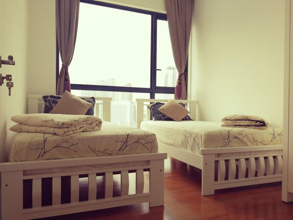 Two twin beds with white frames and matching bedding, a large window with curtains, and a view of buildings outside. - Bochang Homestay (Kuala Lumpur)
