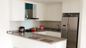 A modern kitchen with white cabinetry, a stainless steel refrigerator, and a built-in island with a coffee maker and a kettle. - Bochang Homestay (Kuala Lumpur)