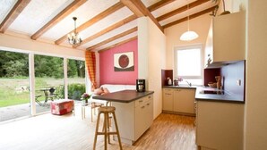 A modern kitchen with wooden beams, a dining area with a table and chairs, and a large window offering a view of the outdoors. - Arrive - holidays - refueling in "House on Forest Park" (Scheidegg-Lindenau)