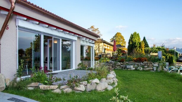 A modern house with a glass door entrance, a stone retaining wall, and a well-maintained lawn. - Arrive - holidays - refueling in "House on Forest Park" (Scheidegg-Lindenau)