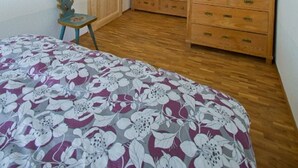 A bedroom with a wooden ceiling, a bed with a floral bedspread, a dresser, a door, and a small table with a vase. - Arrive - holidays - refueling in "House on Forest Park" (Scheidegg-Lindenau)