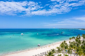 A beach with clear turquoise waters, a sandy shore, and palm trees.
