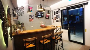 A bar area with a wooden counter and three stools, decorated with wall art and a clock. - Living house (Hengchun)