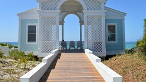 A beach house with a wooden deck and two chairs facing the ocean.