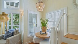 A cozy room with a wooden floor, white walls, a round wooden table with a woven basket, and a staircase with white railings.