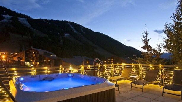 Een bubbelbad op een terras op het dak, met uitzicht op een berg, omringd door lichtslingers en lounge fauteuils.