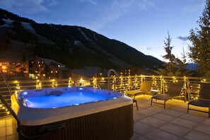 A hot tub on a rooftop terrace with a mountain backdrop, surrounded by string lights and lounge chairs. - Outpost: King Ridge 7 Penthouse - AC & Hot Tub! (Jackson)